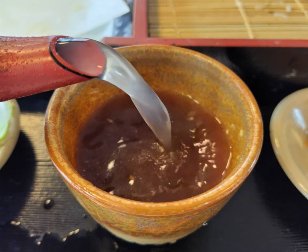 ざるそばの汁に蕎麦湯を入れている写真