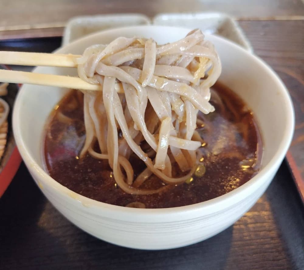 鰹出汁がきいた甘じょっぱいつけ汁に田舎そばを浸している写真