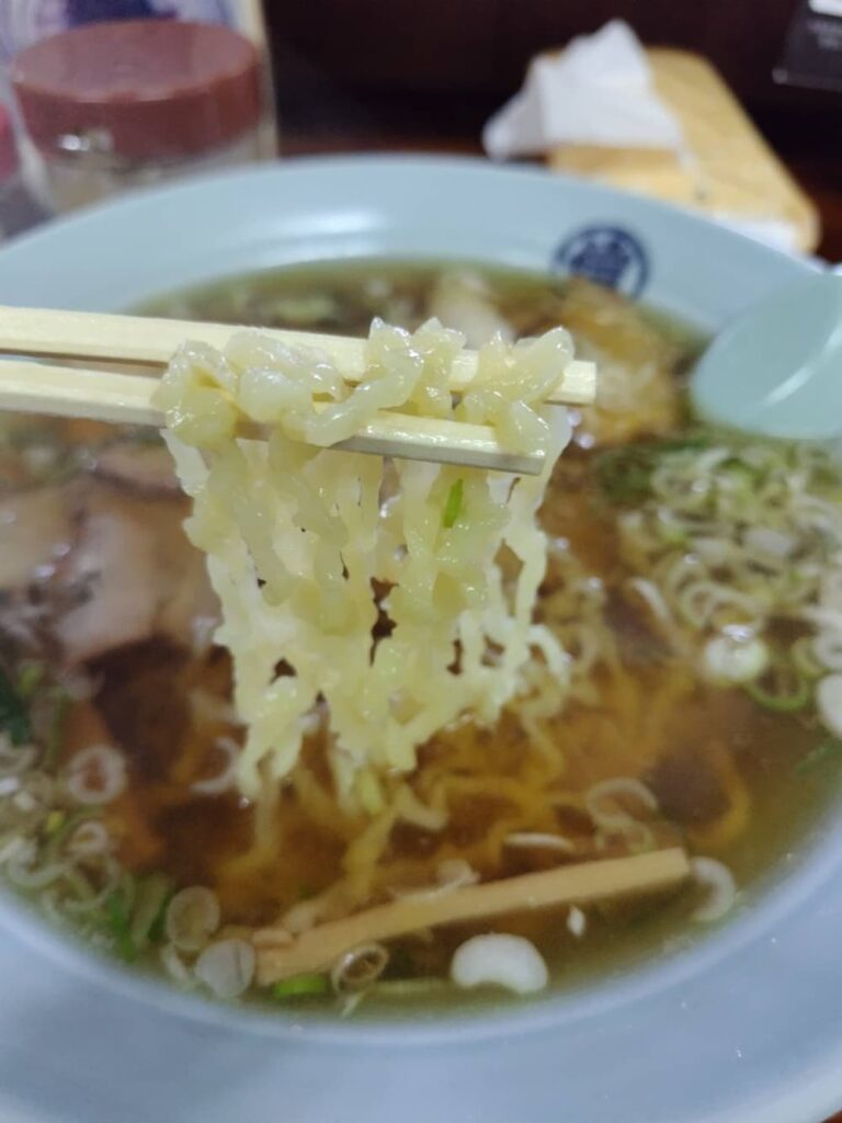 丸信本家の中太ちぢれ麵を箸ですくっている写真