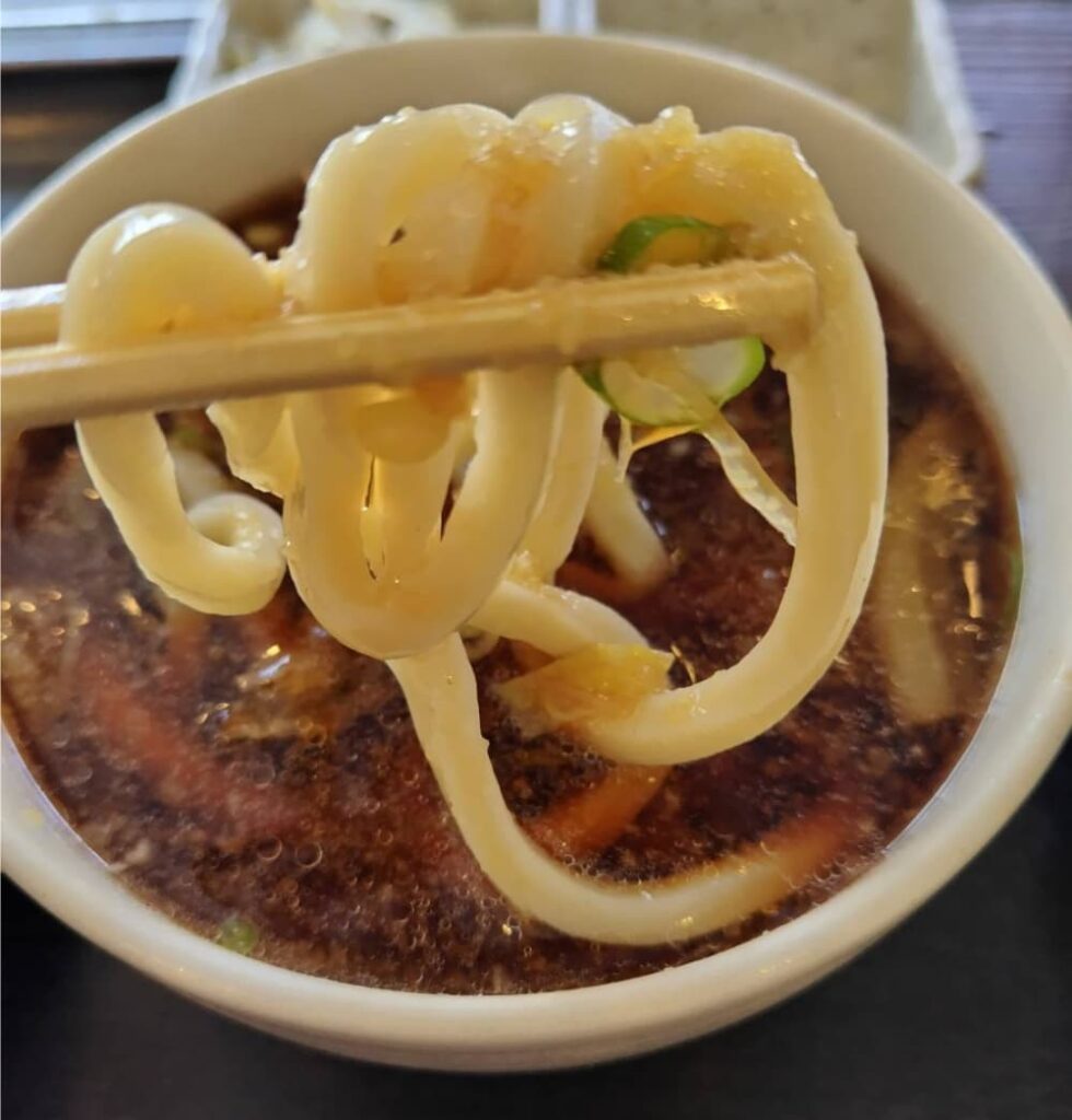 温かいつけ汁にうどんを付けている写真