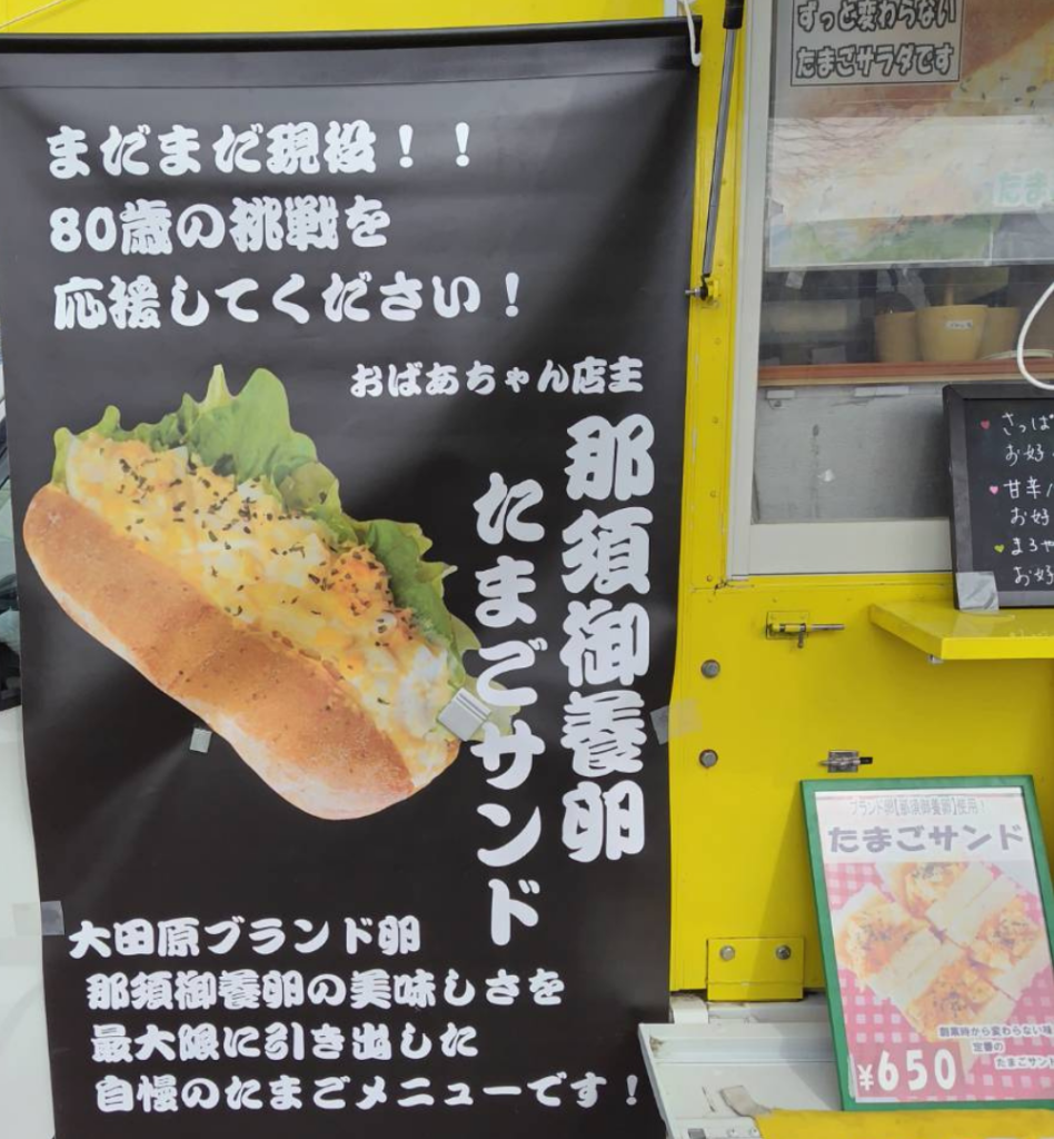 80歳のおばあちゃん店主が挑戦を続けることをアピールした店頭幕の写真