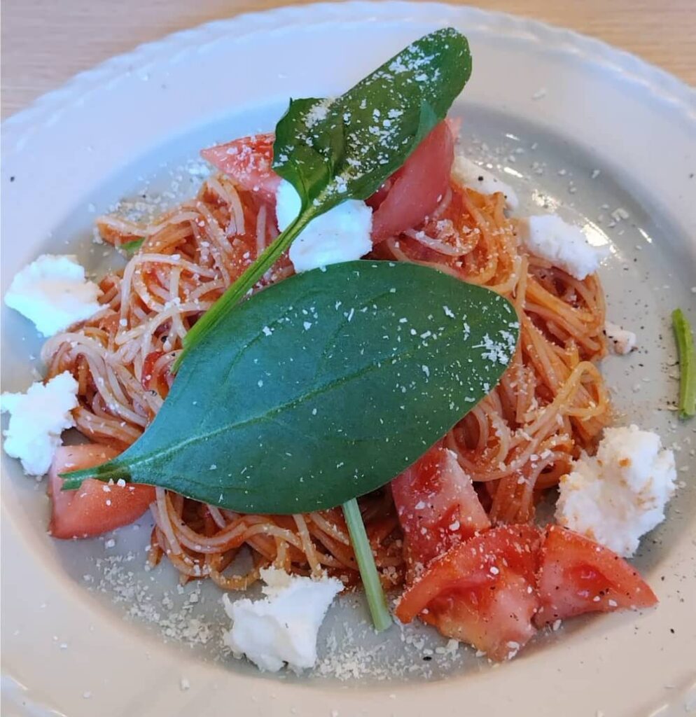 トマトとモッツァレラチーズのスパゲッティに大きめのバジルが乗っている写真