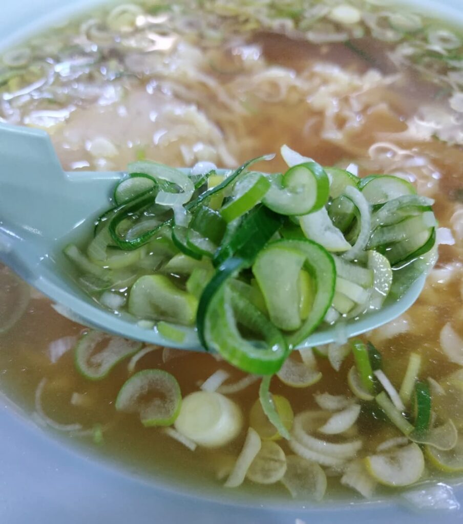 レンゲにトッピングのネギをよそっている様子